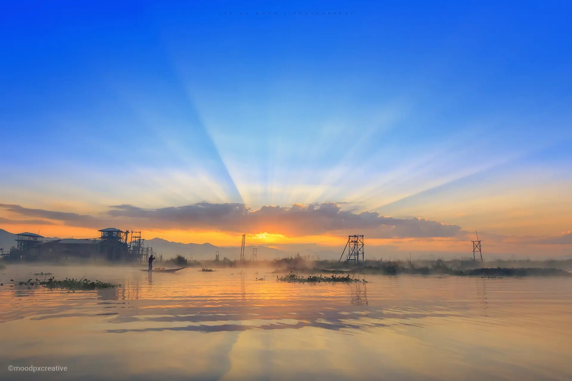 A stunning sun ray breaks through the clouds over Inle Lake, while a leg-rower navigates his boat in the fog.